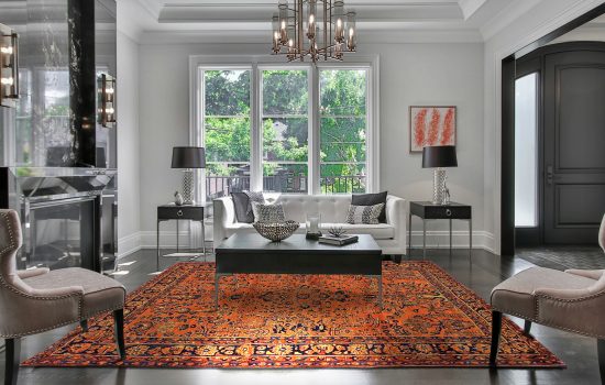 tappeto persiano antico color arancione in soggiorno neoclassico moderno bianco, sotto un tavolino nero e con due consolle ai lati
