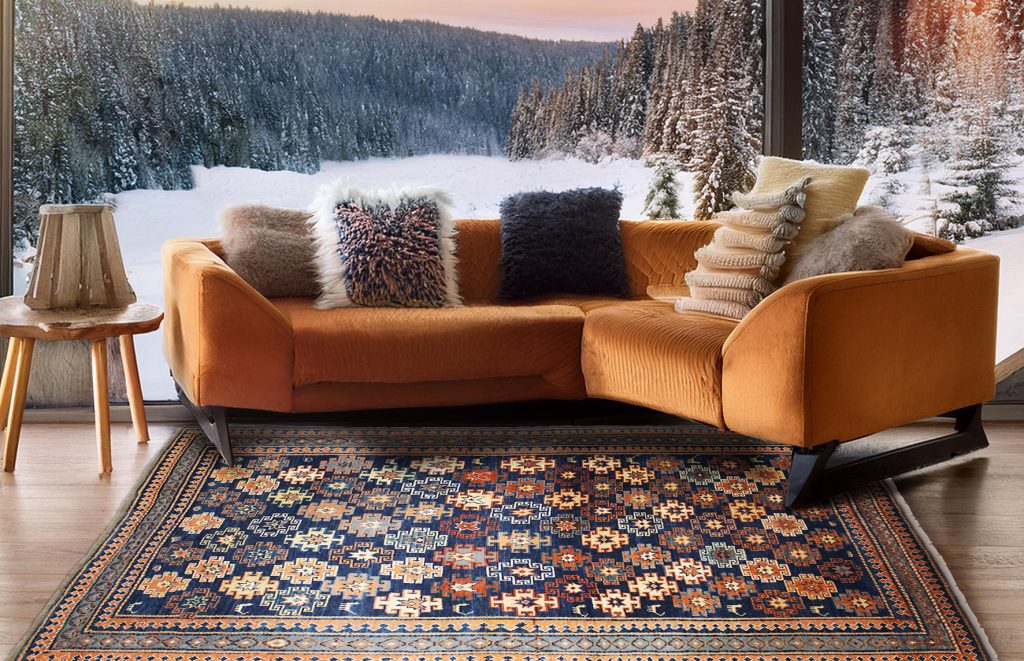 tappeto persiano antico geometrico blu a rombi colorati sotto divano moderno arancione, con grande vetrata che mostra un paesaggio innevato sullo sfondo