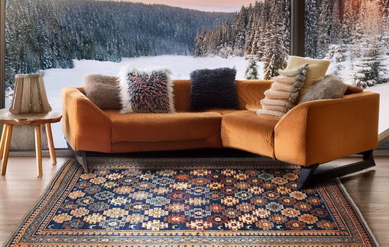 tappeto persiano antico geometrico blu a rombi colorati sotto divano moderno arancione, con grande vetrata che mostra un paesaggio innevato sullo sfondo